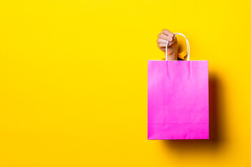 Female hand holds a pink package with purchases on a yellow background