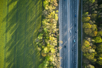 Aerial view of cars driving through the green forest on highway.