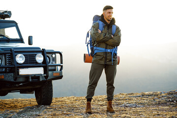 Portrait of a young traveler man in hiking equipment standing near his off-road car