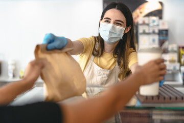 Bar owner working only with take away orders during corona virus outbreak - Young woman worker wearing face surgical mask giving takeout meal to customers - Healthcare and Food drink concept - Powered by Adobe