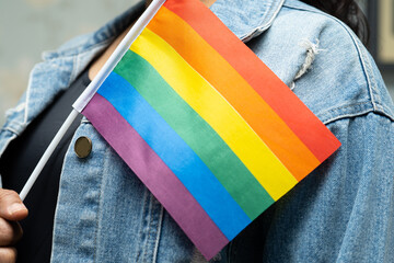 Asian lady wearing blue jean jacket or denim shirt and holding rainbow color flag, symbol of LGBT pride month celebrate annual in June social of gay, lesbian, bisexual, transgender, human rights.
