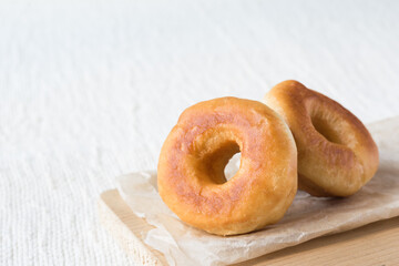 Two donuts on a paper on light rustic textile background, horizontal orientation, copy space