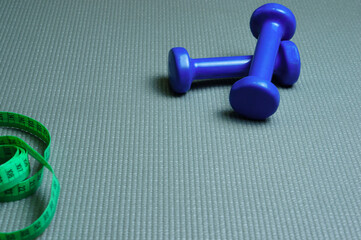 Two blue dumbbells and a waist ruler on a yoga mat in the gym. Sports, fitness, weightlifting, healthy lifestyle. Exercises in the fitness room. Slim body, shape maintenance