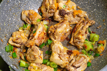 pieces of chicken are fried in a pan with herbs