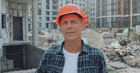 Handsome builder in hard hat smiling at camera on construction site