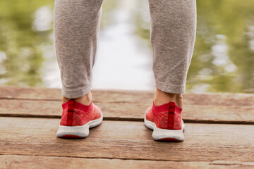 children feet dress  gray pants and red sneakers stand wooden bridge against the background of water