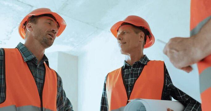 Selective focus of builders with blueprint talking on construction site