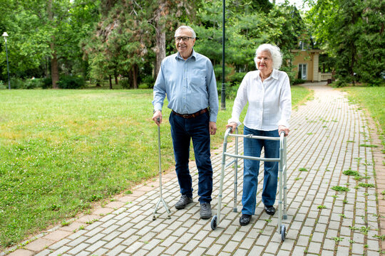 Senior man using a walking cane accompanied by a senior lady strolling with folding walker