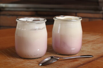 Yogurt in open small glass jar with spoon on wooden cutting boar