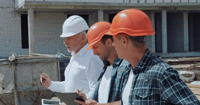 Engineer and builders with equipment talking while walking on construction site