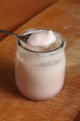 Spoon with yogurt on open small glass jar on wooden cutting boar