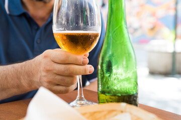 Male hand holding glass of beer on a sunny day. Detail of man enjoying a green bottle beer.