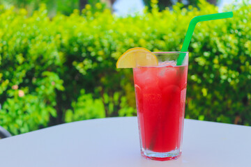 Ice juicy exotic cocktail on the table against the background of blurred greenery. Summer vacation concept. Copy space for text