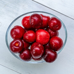 ripe cherries in a glass bowl on a white wooden background