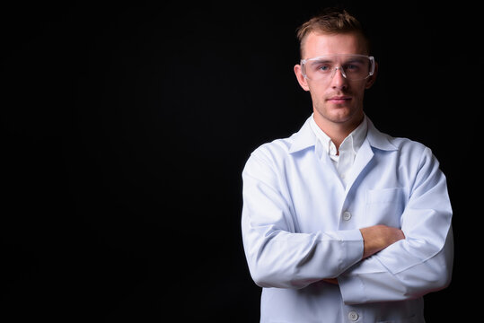 Portrait of young handsome man doctor as scientist with protective glasses