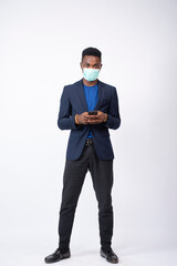 young black businessman wearing a suit and face mask using his mobile phone