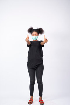 A Young African Lady Wearing A Face Mask Giving Thumbs Up With Both Hands