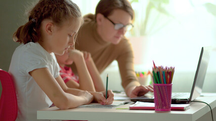 Cute children use laptop for education, online study, home studying, Boy and Girl have homework at distance learning. Lifestyle concept for home schooling. Mother helps daughter and son.