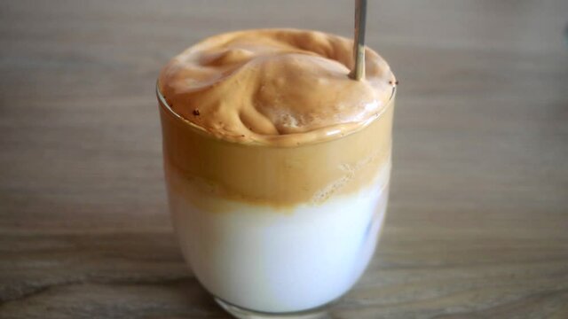 coffee latte in glass. iced coffee with ice cream. Whipped coffee stirring by spoon. glass of milk ready to drink. Close view of a glass of coffee stirring with steel spoon.  