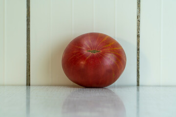 Red tomato with gray spot and yellow stripes reflex in light table. Organic vegetables is good for healthy diet, because contains a lot of vitamins and minerals. Horizontal picture, copy space.