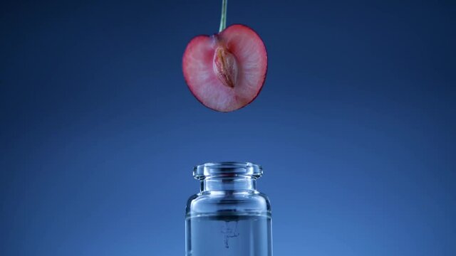 Closeup drop of cherry oil for spa procedure falling from berry into glass bottle against blue background