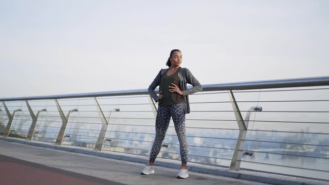 extra long shot. A girl African American athlete stands on a glass bolkon and does exercises for the legs and hip joint. 4K