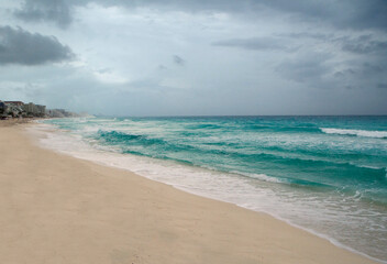 Vacations in Cancun. Seascape. Beautiful view of the white sand shore, turquoise water ocean, sea waves and coastline under a cloudy sky. 