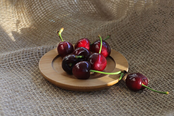 ripe juicy red cherry berries on a wooden plate on a rough sacking