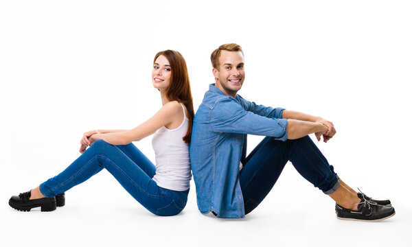 Smiling attractive happy couple. Full body length profile portrait image of sitting back to back models in love studio concept, isolated against white background. Man and woman posing together.