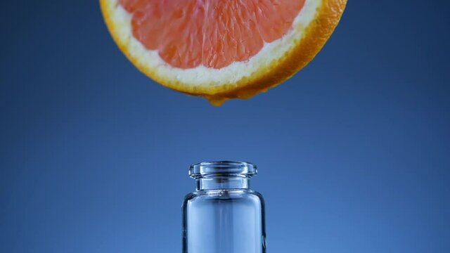 Closeup essential oil of grapefruit falling into glass bottle of perfume on blue background