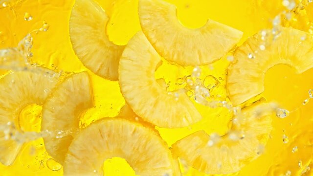 Super Slow Motion Shot of Pineapple Slices Falling into Water on Yellow Background at 1000fps.