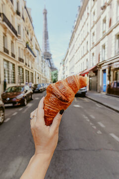 Hand holding croissant in parisian street with Eiffel tower view