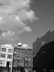 A moody New York City street view with old apartment buildings, rooftops and clouds in black and white. 