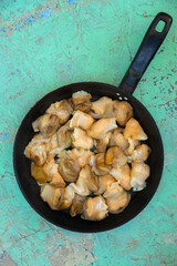 Chopped raw rapana (Rapana pontica) meat in a frying pan on a blue concrete background, close-up.