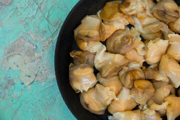Chopped raw rapana (Rapana pontica) meat in a frying pan on a blue concrete background, close-up.