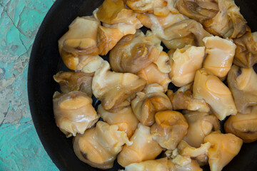 Chopped raw rapana (Rapana pontica) meat in a frying pan on a blue concrete background, close-up.