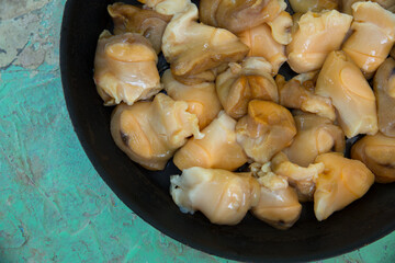 Chopped raw rapana (Rapana pontica) meat in a frying pan on a blue concrete background, close-up.