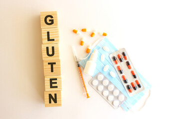 The words GLUTEN is made of wooden cubes on a white background with medical drugs and medical mask. Medical concept.
