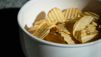 Close up and isolated photo of rustic potato chips in a white ceramic bowl. Concept photo for snacks and unhealthy foods.
