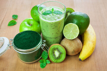 Zielone smoothie w szklance otoczone owocami i spiruliną w słoiku © Monika