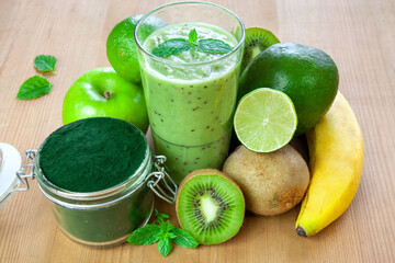 Zielone smoothie w szklance, obok owoce i spirulina