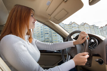 Young redhead woman driver behind a wheel driving a car smiling happily.