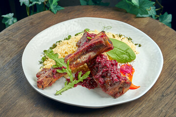 Appetizing grilled pork ribs with bulgur in a white plate on a wooden background. Selective focus. Roasted ribs