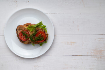 sandwich with cutlets lettuce and tomato slices on a plate on white background