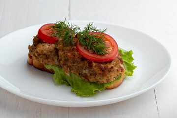 sandwich with cutlets lettuce and tomato slices on a plate on white background