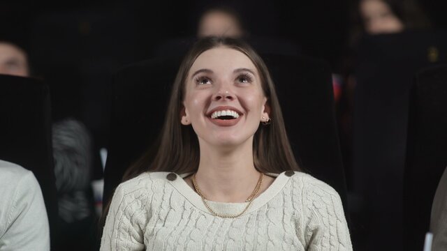 A young woman at the movies begins to smile and laugh