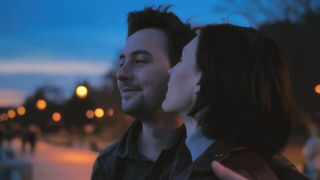 Close-up portrait of a beautiful young couple on the street of the night city against the background of colorful lights. Love story, romantic atmosphere. Two lovers hug and watch the sunset. A woman