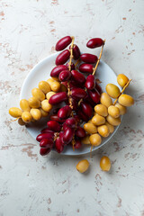 fresh dates fruit on textured white background , red and yellow fresh dates fruit in white plate