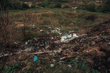 Large pile of garbage in the countryside. Pollution of nature with plastic waste. Green land full of rubbish. 
Dirty trash dump in the village. Scattered litter in the vicinity.
