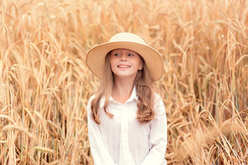 Obraz premium Happy child in wheat field. Beautiful girl with white hair in a straw hat with ripe wheat